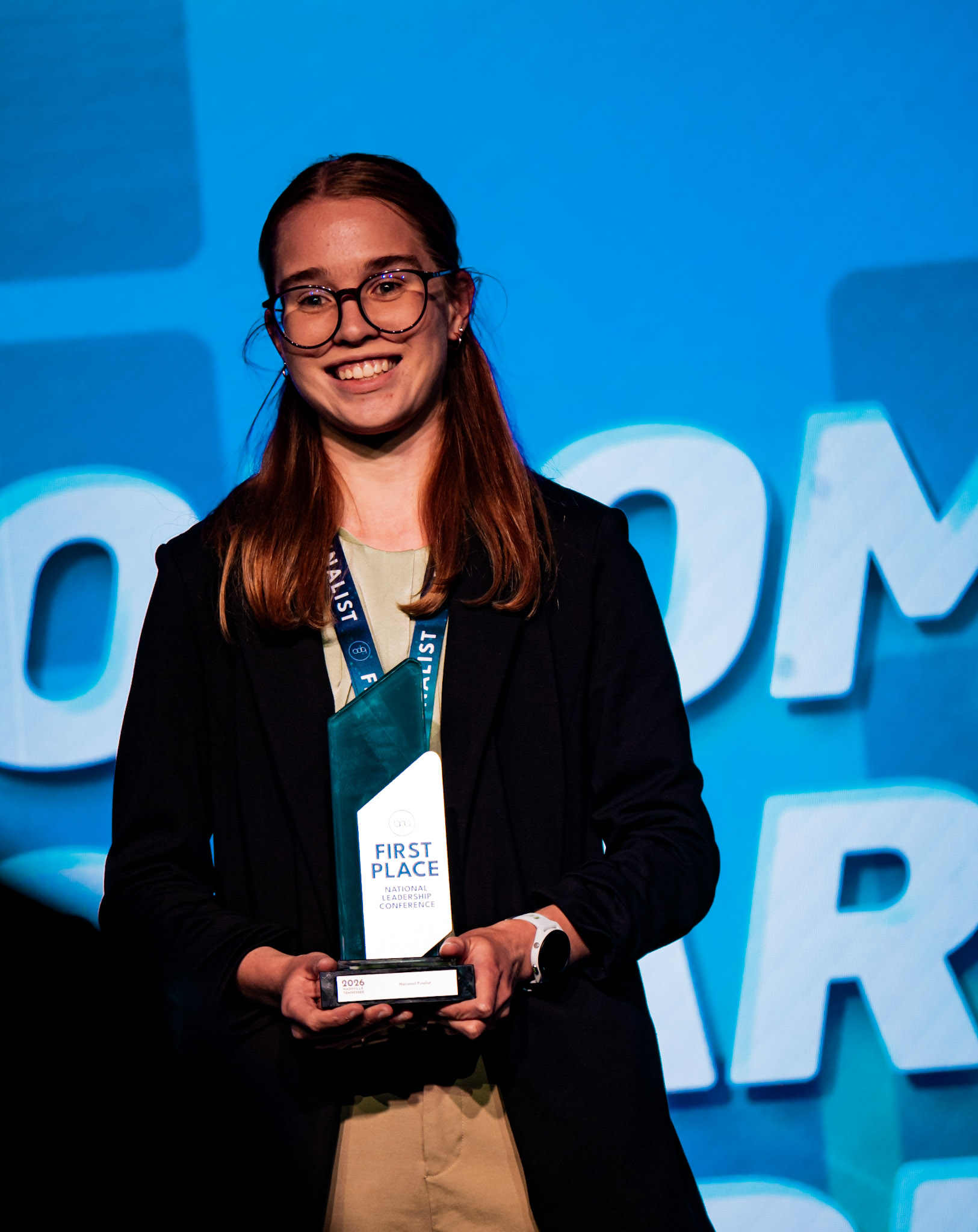 Woman in black coat holding First Place NLC trophy on stage