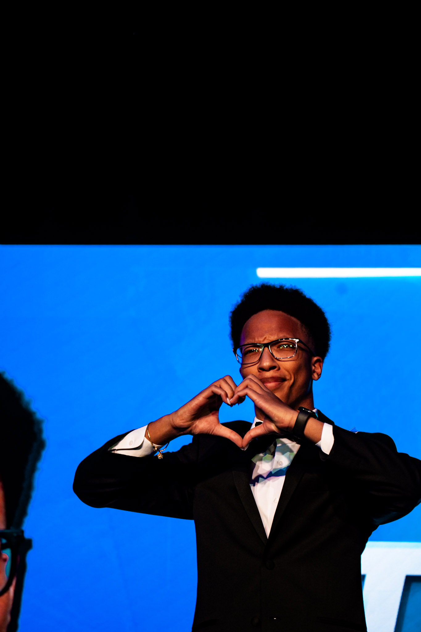 Person in tuxedo making a heart sign on stage — BPA NLC