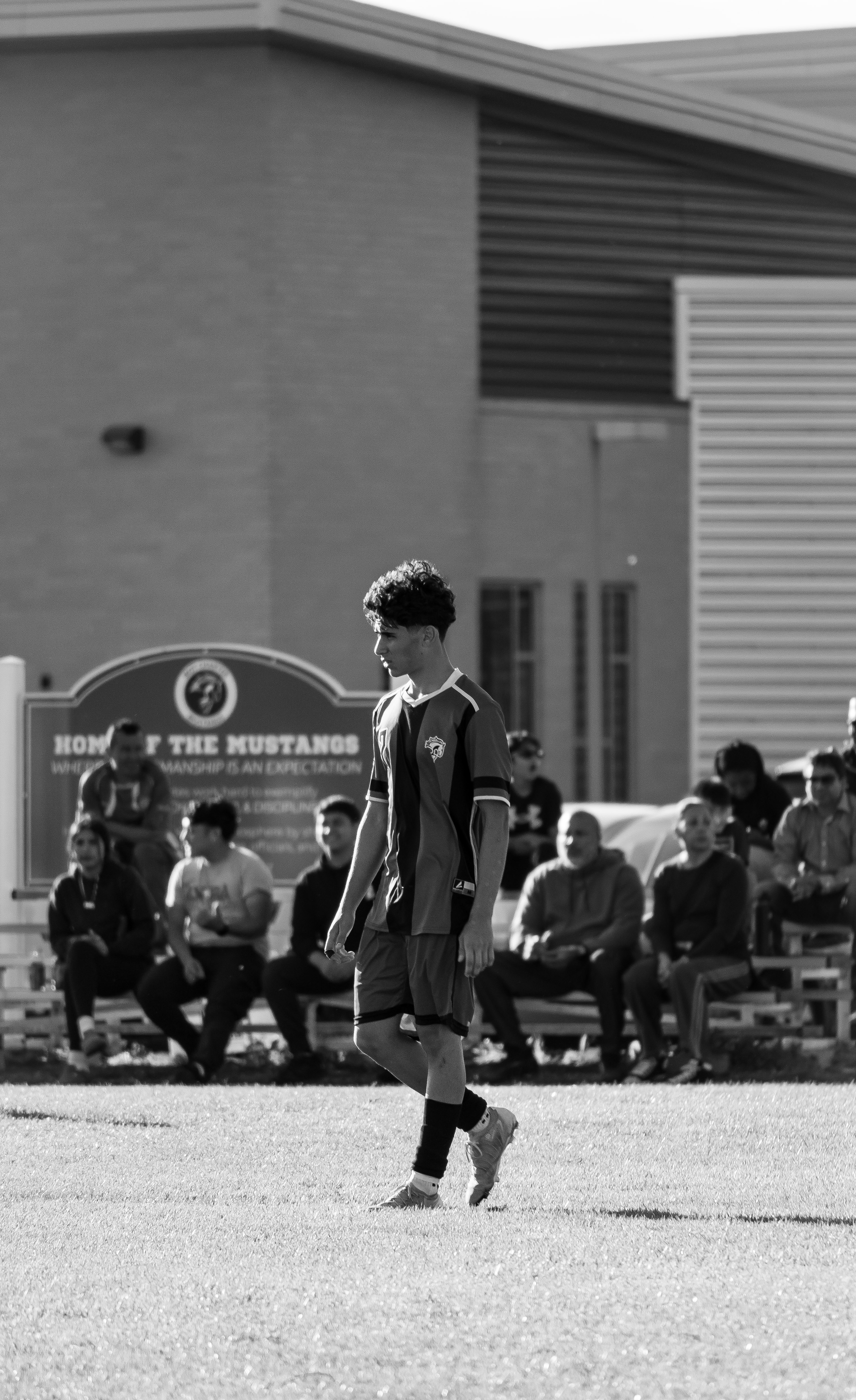 Soccer player walking on field in black and white â€” Home of the Mustangs sign