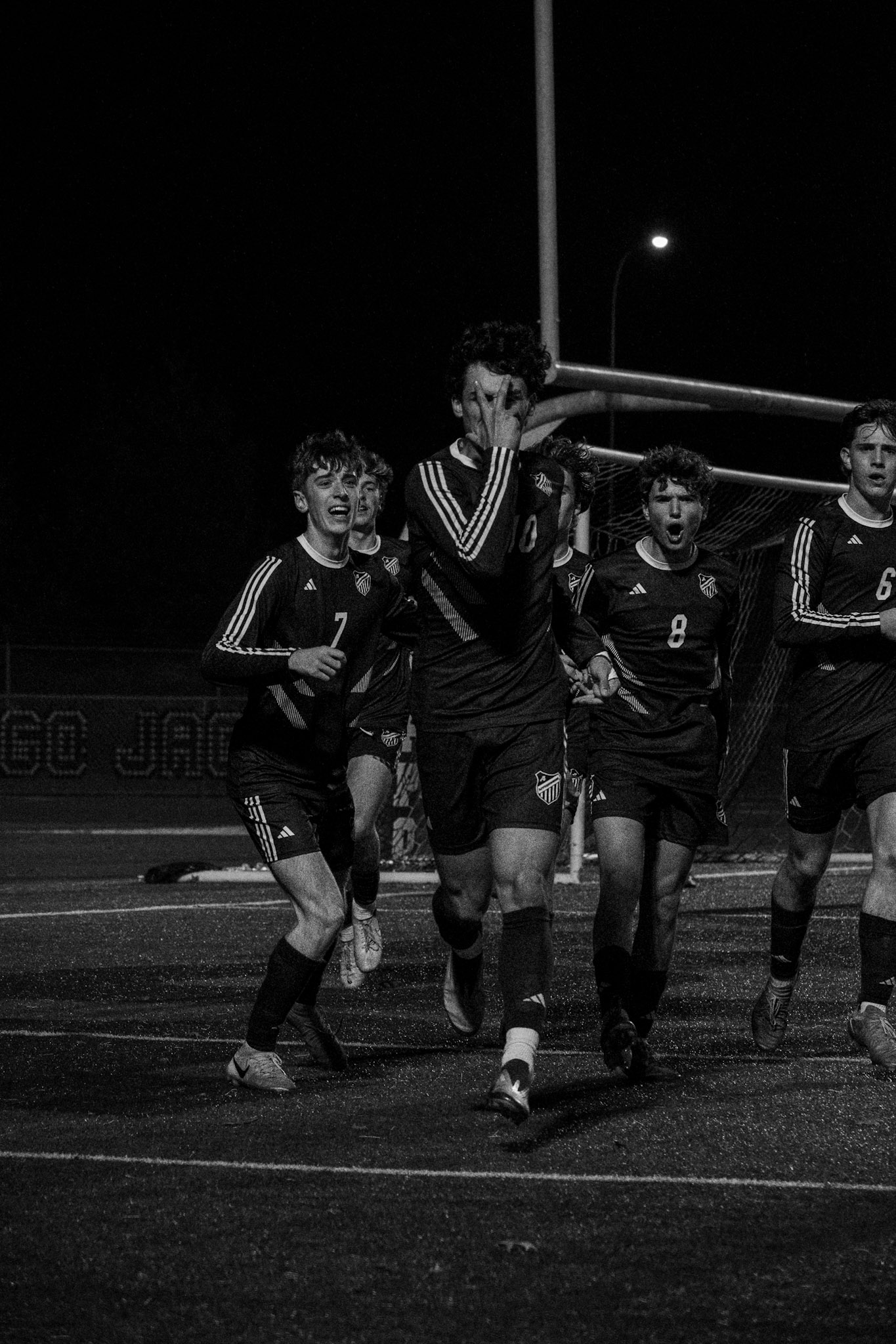 Soccer players celebrating a goal on field at night — black and white